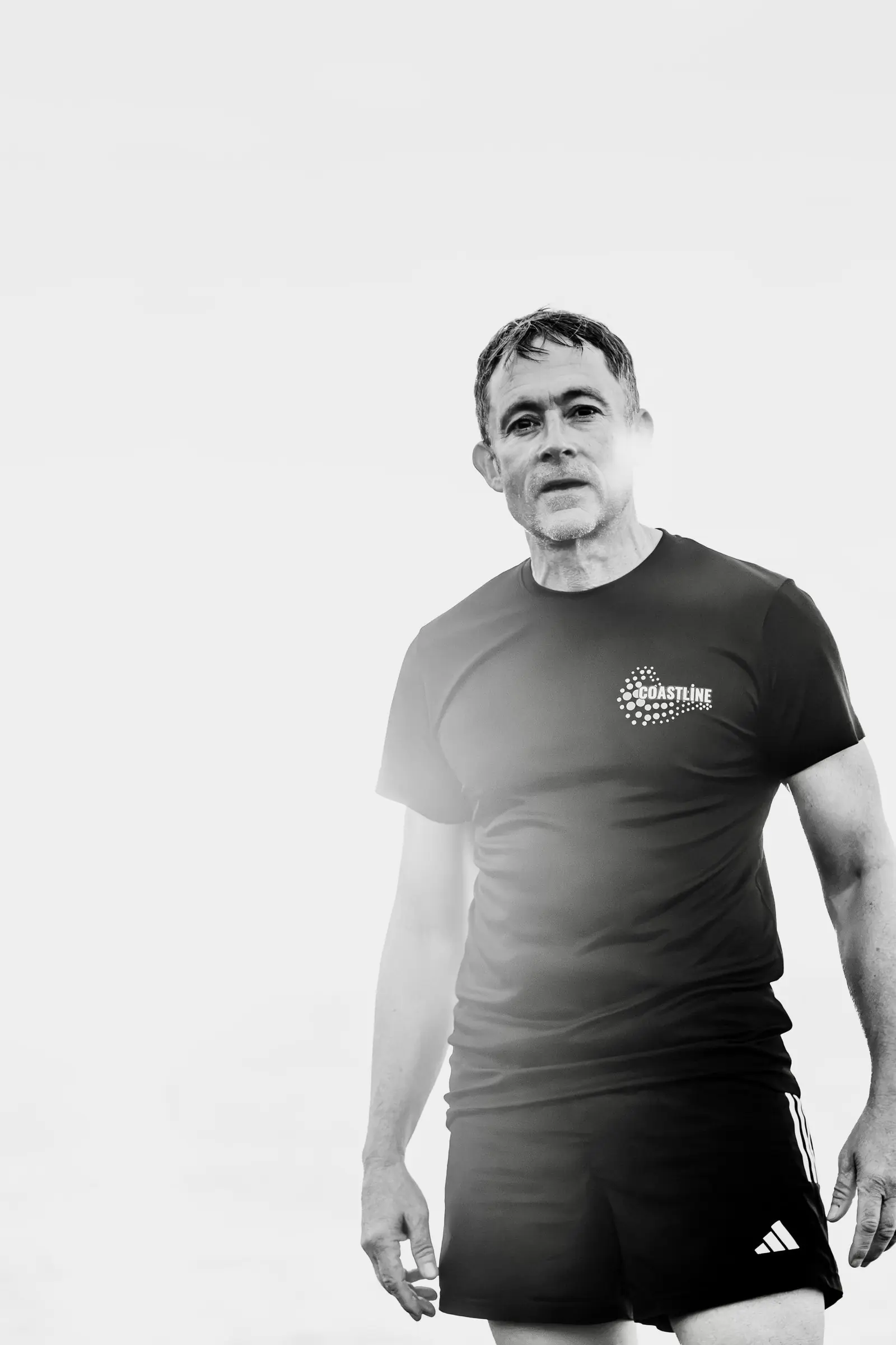 Black and white portrait of Mark standing on the beach in a Coastline T-shirt
