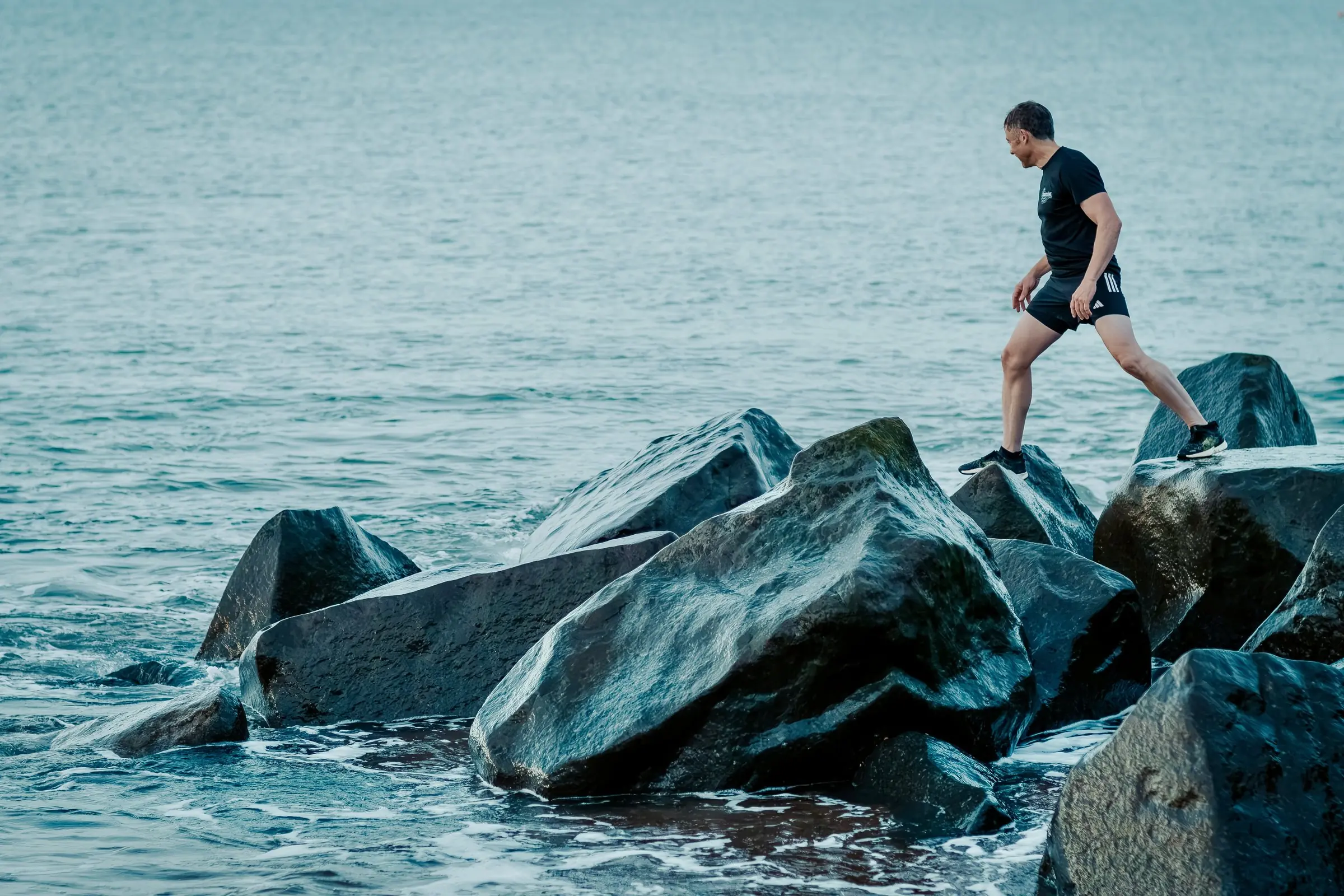 Mark stepping carefully across wet rocks at the water's edge
