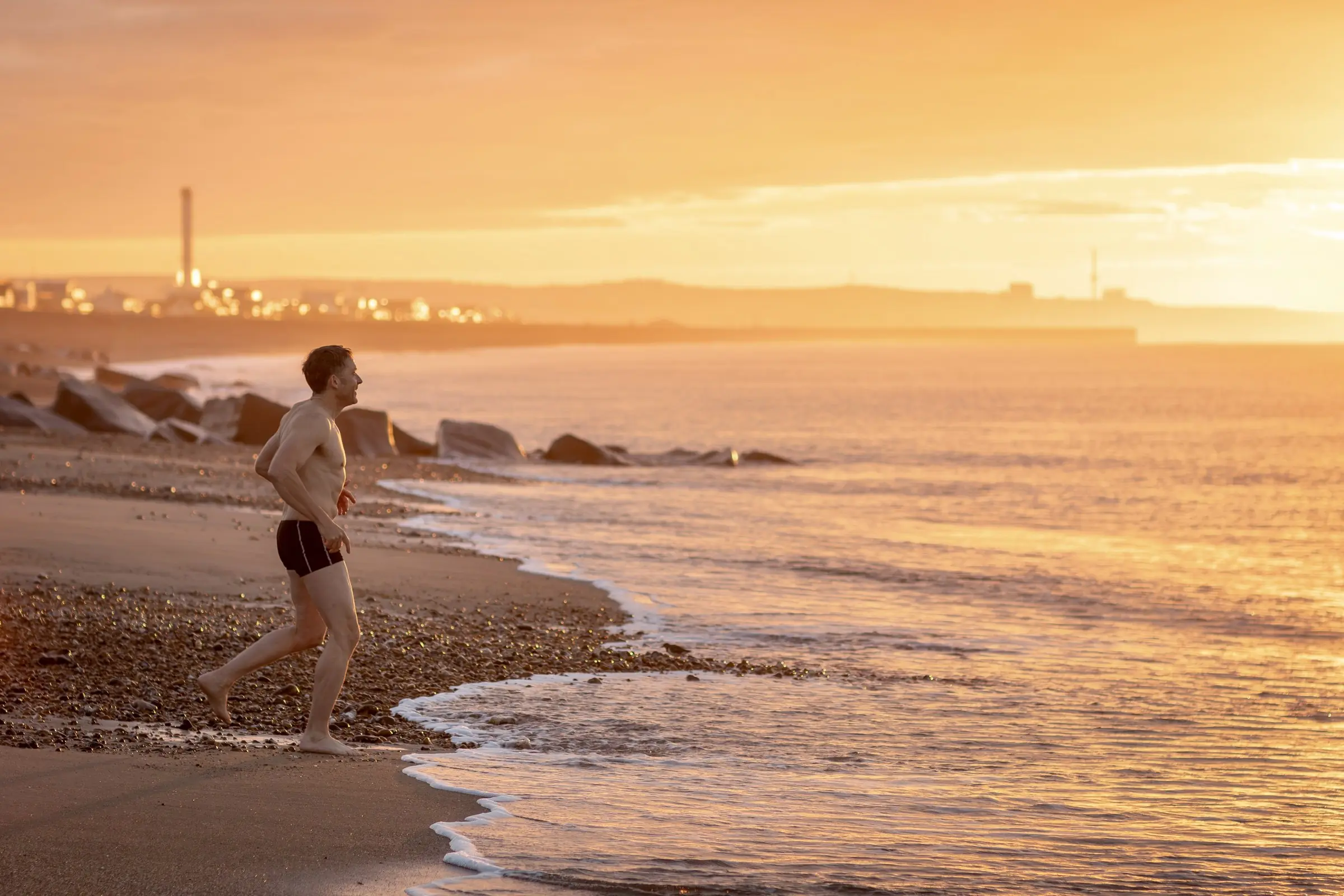 Mark walking along the water's edge at sunrise, the harbour lights behind him